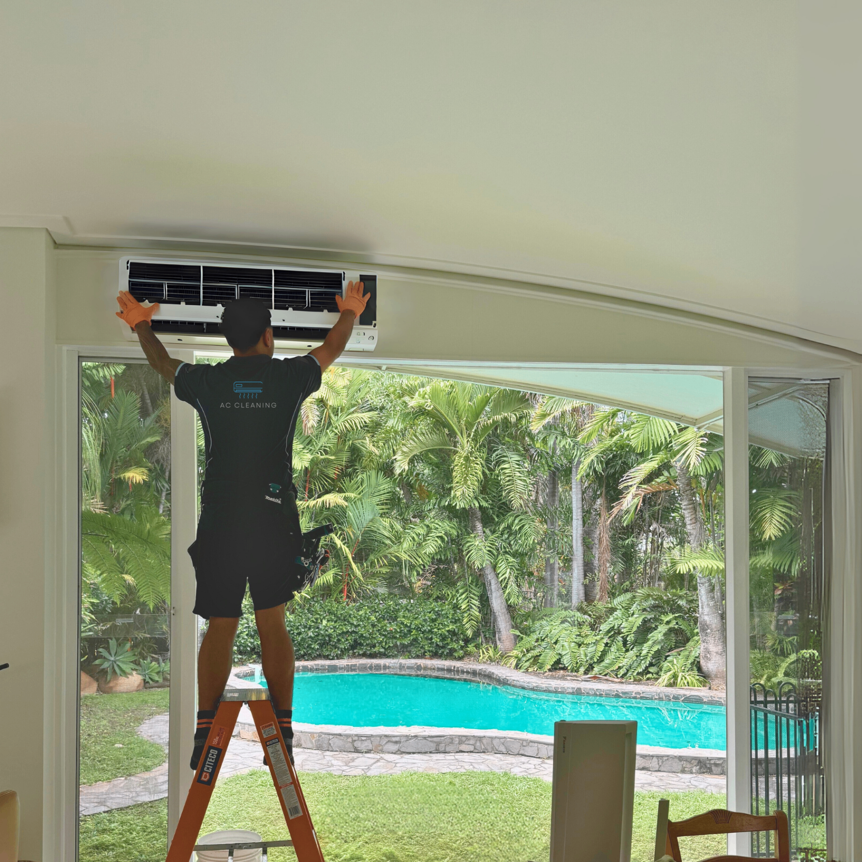Professional AC technician cleaning air conditioning unit with tropical pool background